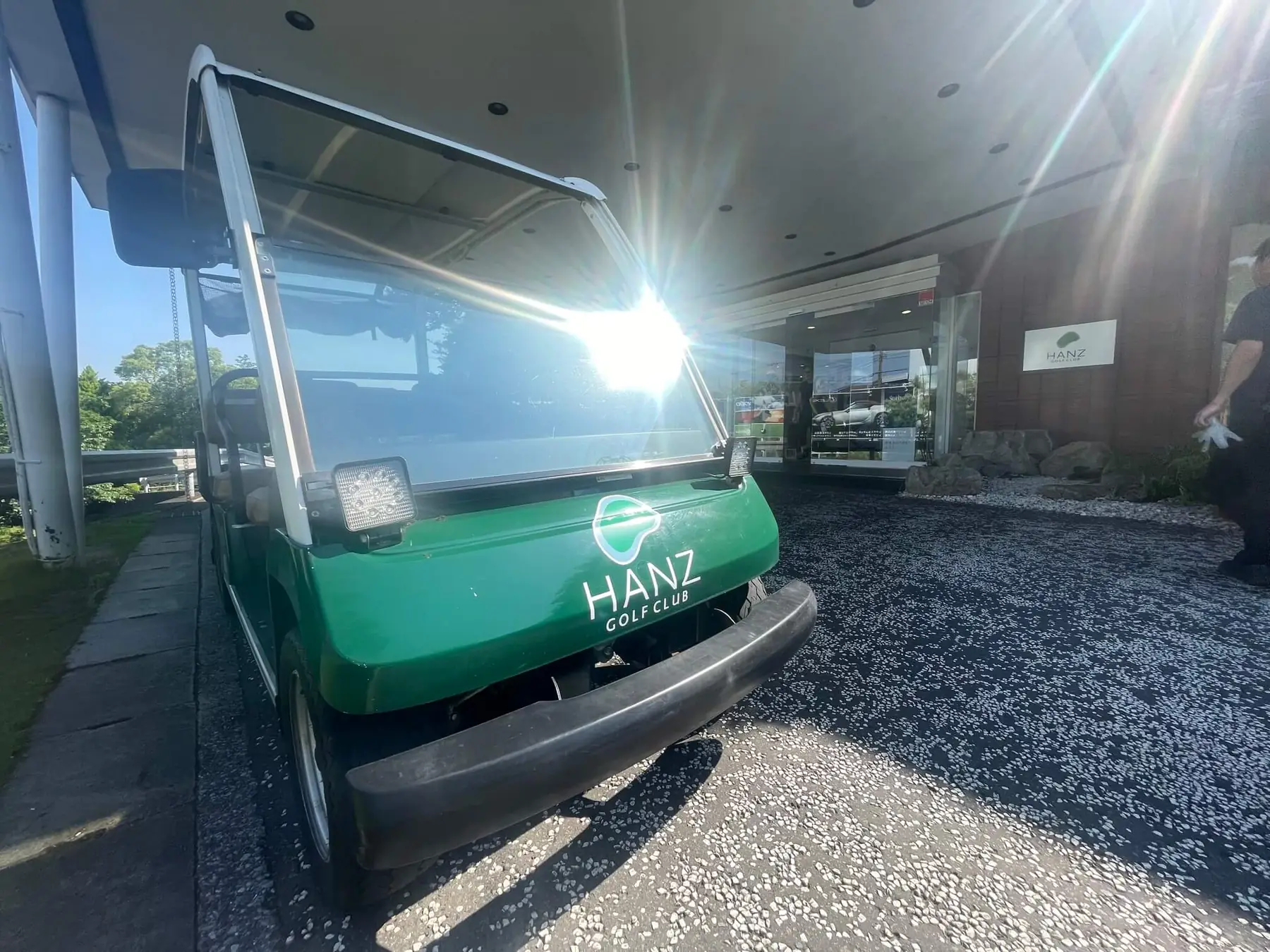 HANZ GOLF CLUBのロゴ入りの緑のカートと、奥のクラブハウス入口。