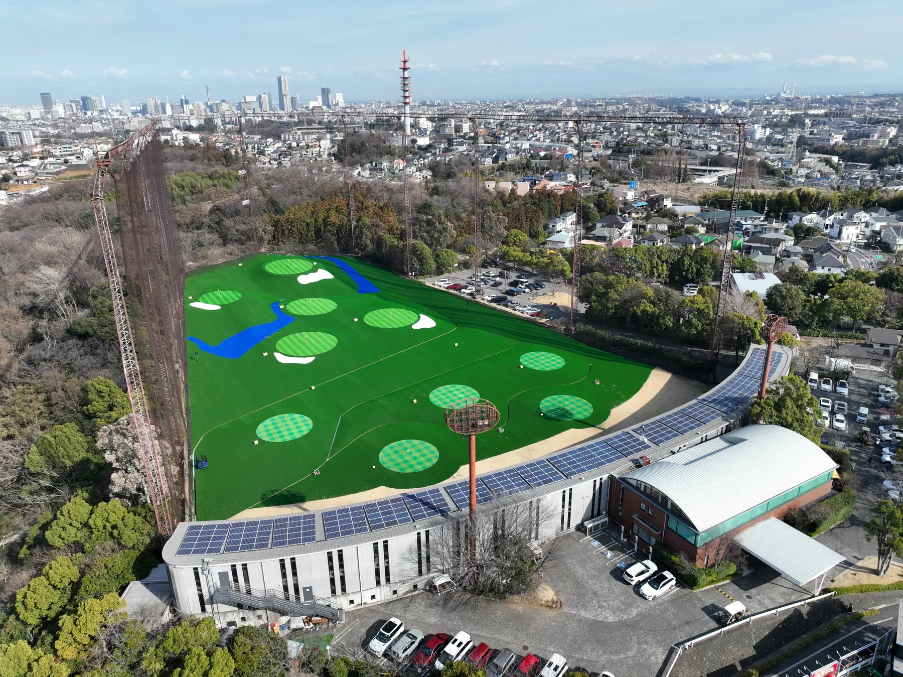 昼のHANZ GOLF CLUBのレンジを上空から見た全景。ターゲットグリーンの置かれた芝の外野と、太陽光パネルの載った打席棟。