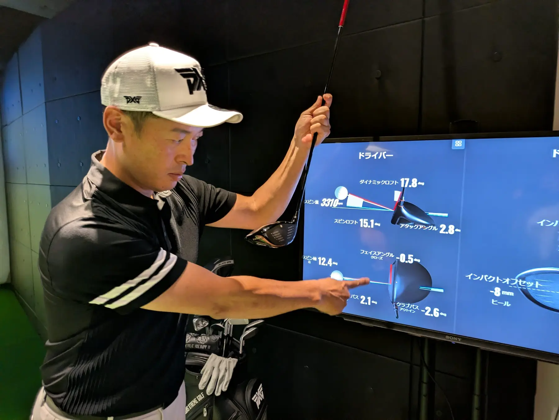 白いキャップの男性がドライバーを持ち、計測データの映ったモニターを指して説明している。